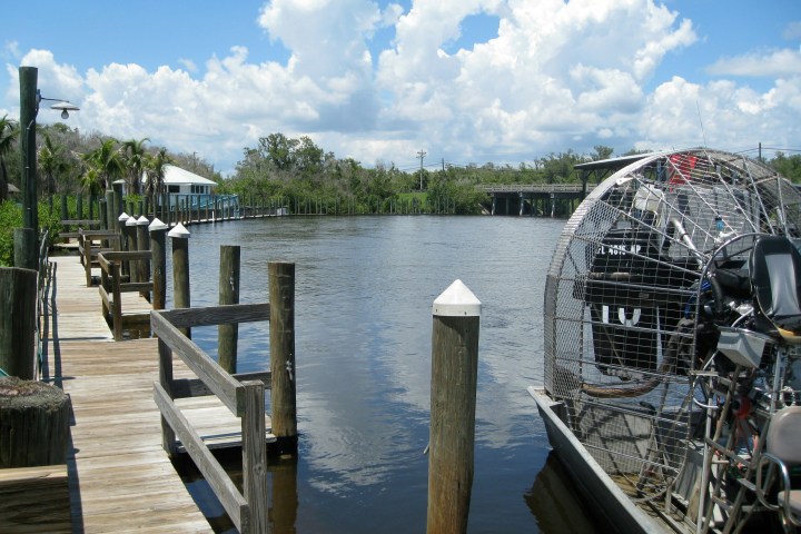 Dock with airboat on a calm river under a cloudy sky.
