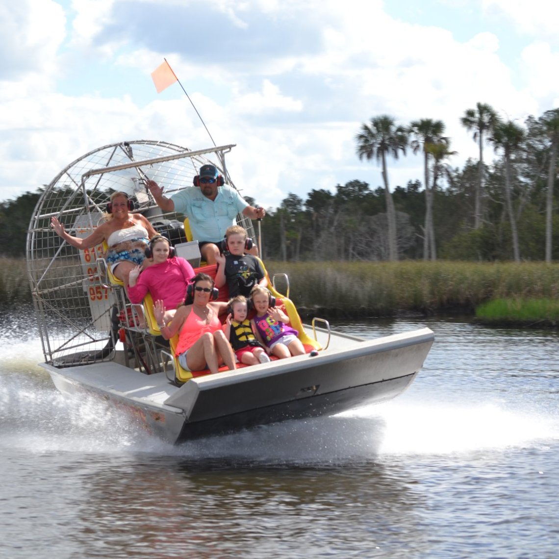 Group riding an airboat on a river, with a forested background.