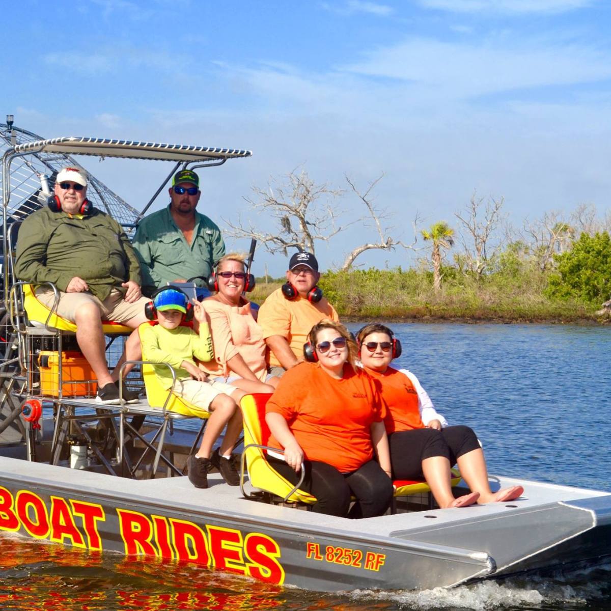 Group on an airboat ride through a marsh with trees in the background.