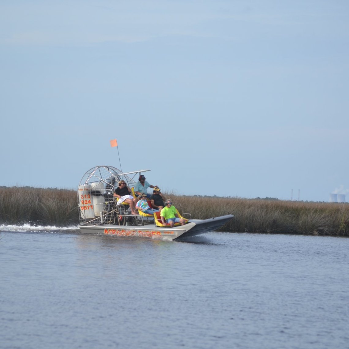 Airboat with passengers travels through marshland on a sunny day.