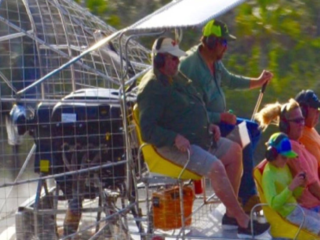 Group of people in bright clothes on an airboat in a marshy area.